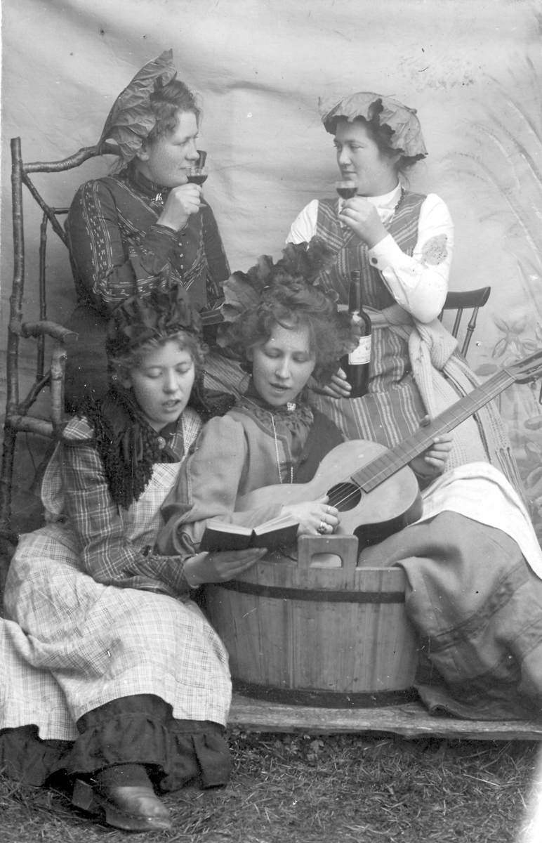 Fire kvinner fra Nesna hos fotograf John Hals ca. 1914. De poserer med stamp, gitar, vin og rabarbrablader på hodet. Bak fra venstre Lina Walnum og Signe Zahl (Lukassen). Foran fra venstre Ragna Walnum (Winther) og Marie Berg (Beck).