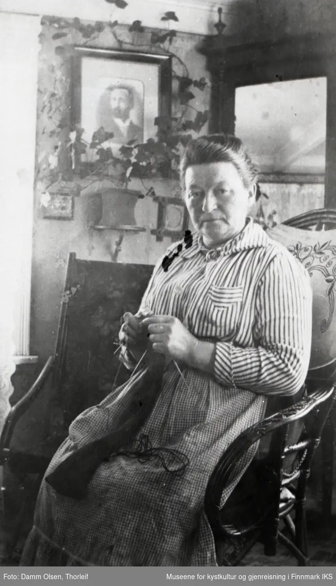 Honningsvåg. Stueinteriør. Johanne Olsen sitter i en kurvstol og strikker. Ca. 1920-27.