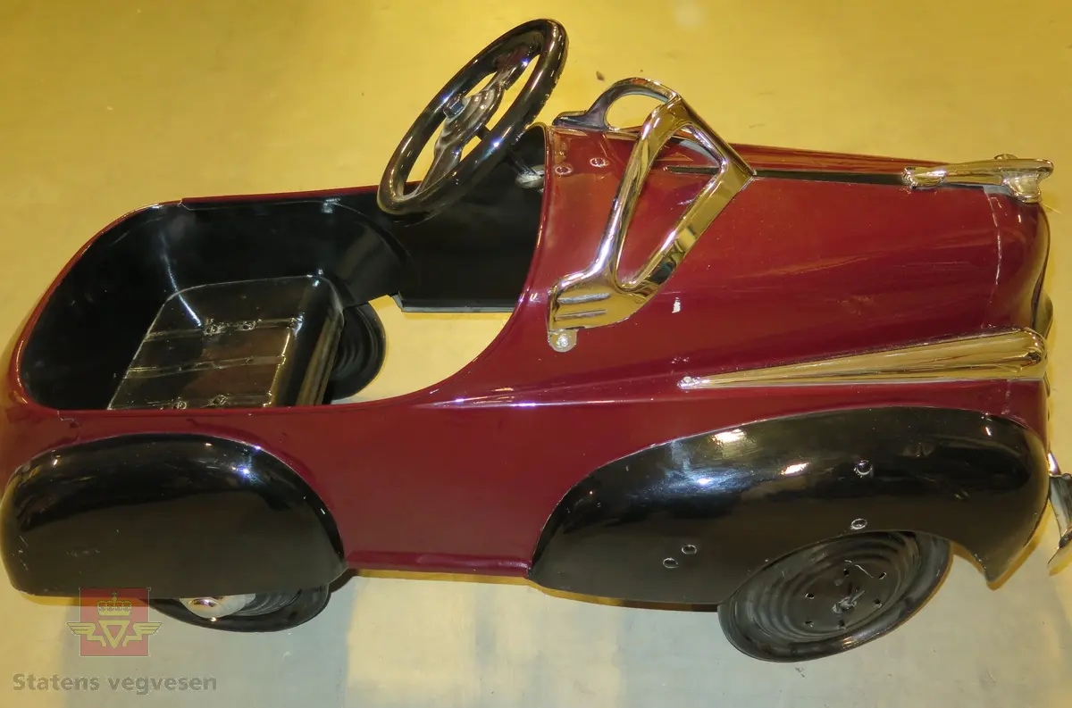 Rødt og svart karosseri av metalll. 4 hjul med hjulkapser, en kapsel mangler, dekk av kompaktgummi.