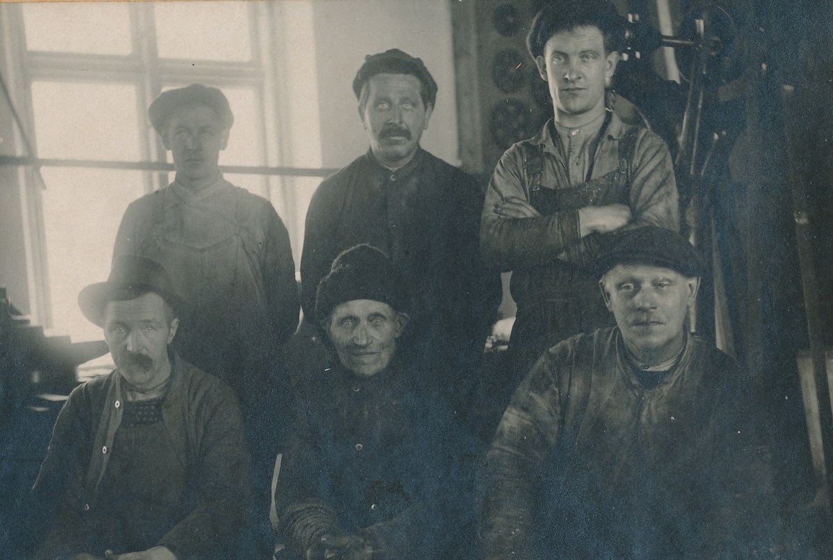 Gruppebilde av arbeidskledde menn i mekanisk verksted.