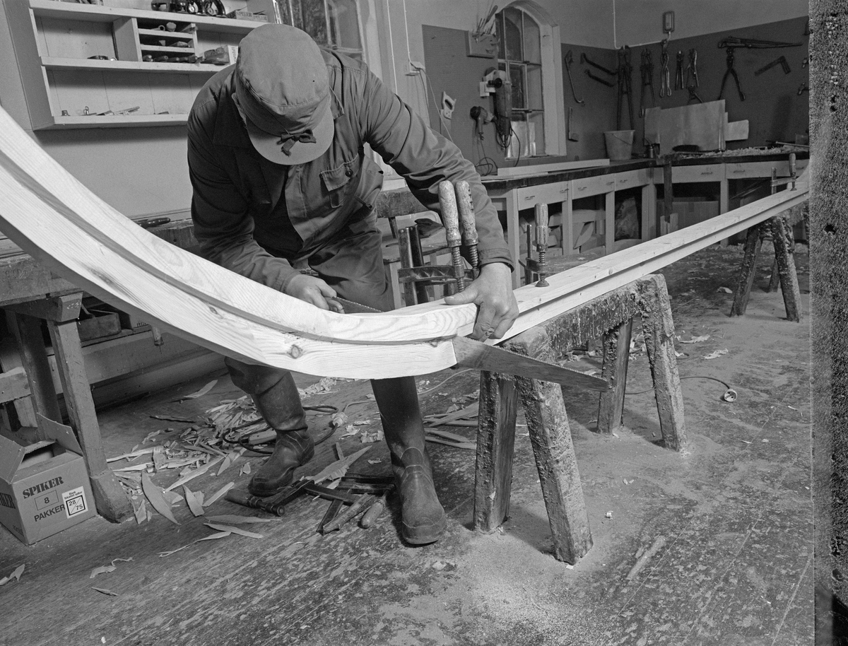 Bygging av fløterbåt i Glomma fellesfløtingsforenings verksted Breidablikk ved kommunesenteret Flisa i Åsnes i november 1984. Båttypen ble for øvrig kalt «Flisabåt», men denne modellen var egentlig utviklet av John Dybendal (1904-1985) omkring 1930. Målet var å kunne levere en robåt som passet i elva Flisa. Dybendal bygde sjøl slike båter fram til 1949. Glomma fellesfløtingsforening hadde vært en viktig kunde hos Dybendal, og da han gav seg som båtbygger ble virksomheten flyttet til denne virksomhetens verksted for Solør-regionen, hvor båtbygging ble vinteraktivitet for et par av karene som hadde vassdraget som arbeidsplass sommerstid. Det var maler til alle båtdeler, og skroget ble bygd på tverrmaler som ble festet til kjølen. Dette var hjelpemidler som gjorde det mulig for fløtere med reletivt liten håndverkserfaring å bygge denne båttrypen og oppnå den standardiserte formen som fløterkameratene var vant med. De fleste flisabåtene fikk jernspanter, for det var krevende å finne de krokvokste emnene som gav de beste spantene. Ettersom Norsk Skogbruksmuseum dokumenterte båtbygginga ville karene likevel bruke trespanter. Da dette fotografiet ble tatt tilpasset Lars Bernhard Olastuen (1927-1998) en av stevnene til kjølen. 

Båten som var under bygging da dette fotografiet ble tatt ble seinere overlatt til Norsk Skogbruksmuseum, der den fikk nummer SJF.07823 i gjenstandssamlinga. Den er 518 centimeter lang og 153 centimeter bred. Odd Jensen har seinere lagd oppmålingstegninger, som også finnes i museets arkiv.