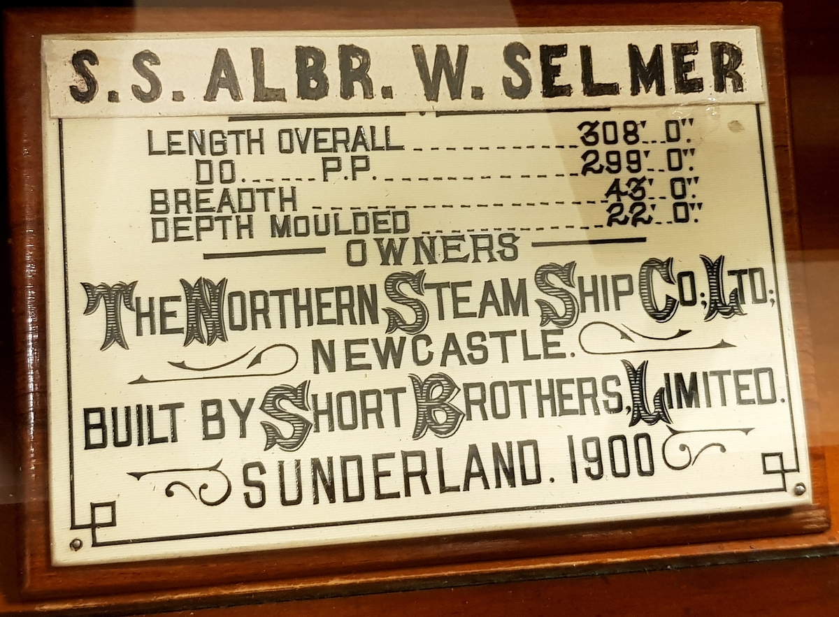 En halvmodell av et dampskipet "Saltwell", senere "Albr.W.Selmer", i en glassmonter til oppheng på vegg. På bakveggen i monter er det en speilvegg.