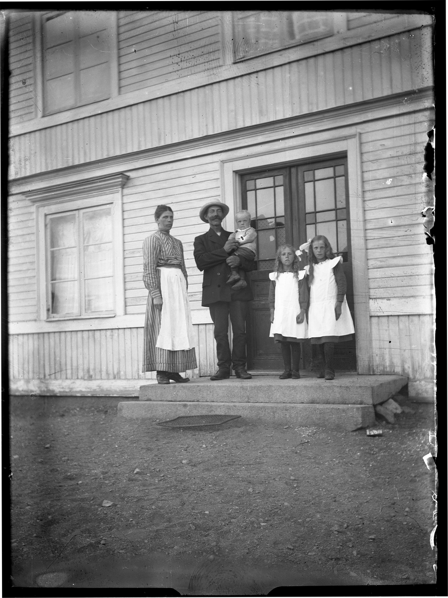 Par med tre barn, stående på trappa till hus.
