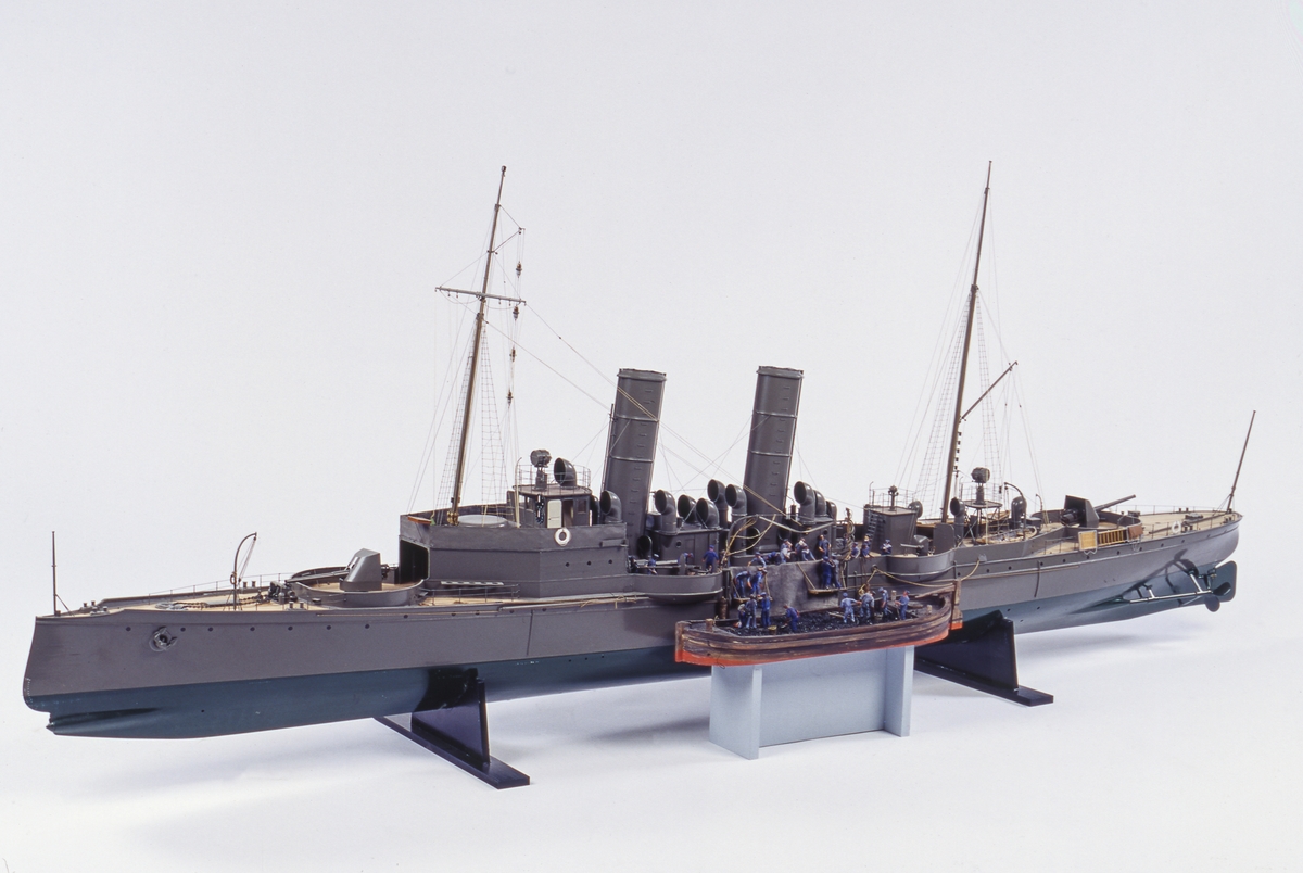Fartygsmodell, torpedkryssaren Psilander, skala 1/32. Byggd av hoplimmat virke och sedan urskölpt. Undervattenskropp grönmålad, övervattenskropp och överbyggnad gråmålade. Ribbdäck. 2 propellrar. Rigg med stående och löpande gods. 2 st. 12 cm:s kanoner, 4 st. 57 m/m kanoner. Till skeppet hör flera mindre båtar:
En slup, 8-huggare med 8 st åror, 2 st. båtshakar och roder med rorkult (se bilder).
En slup,  4-huggare med 4 st åror, 2 st. båtshakar och roder med skädda.
1 joll för 4 åror med 4 st åror, 1 st båtshake och roder med rorkult.
1 ångslup med 2 åror och 2 båtshakar.
2 st. fallrep
2 st. ankare.
Flaggspel och gösstake utan flaggor. Vimpel å stortoppen. Skrå i form av 2 mässingspelare.
Längd: ö.a.: 226 cm Bredd: 24.2 cm Höjd utan skrå: 80 cm (stormasten).