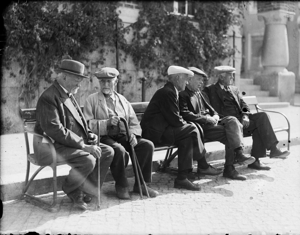Fem äldre män sitter på parkbänk vid Rådhustorget, Östhammar, Uppland