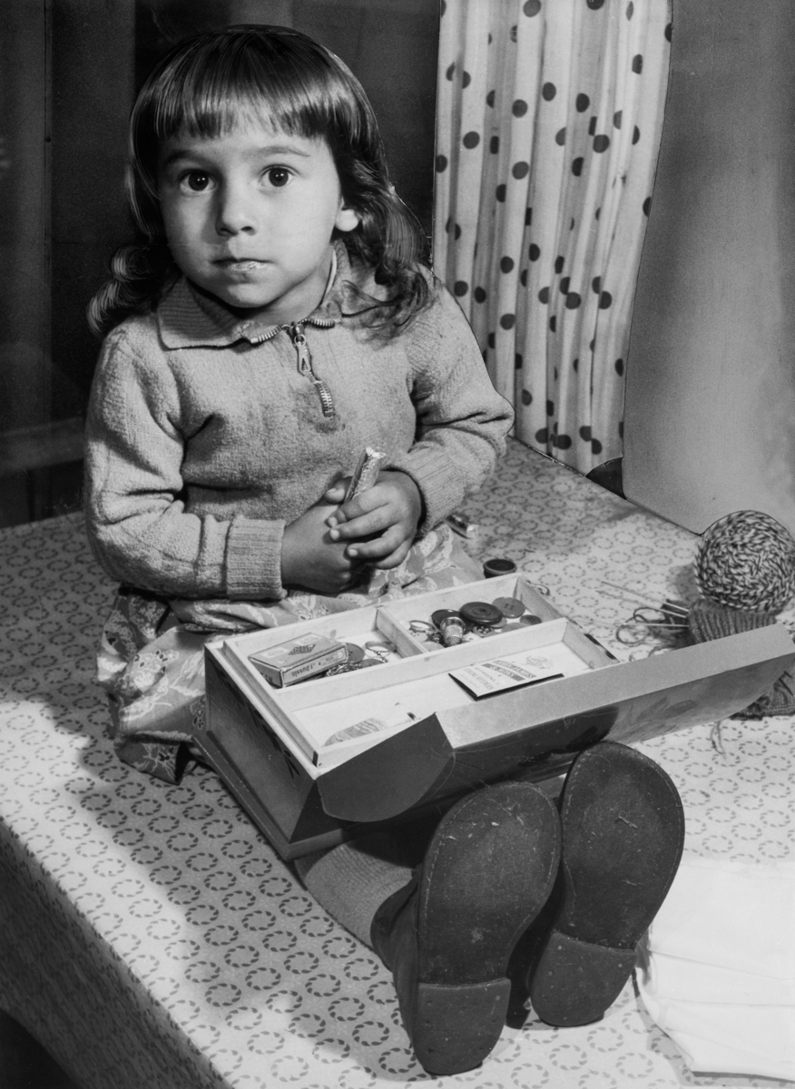 Sömnadsundervisning vid sommarskola för svenska romer, 1952. En liten flicka sitter med ett syskrin i knät.