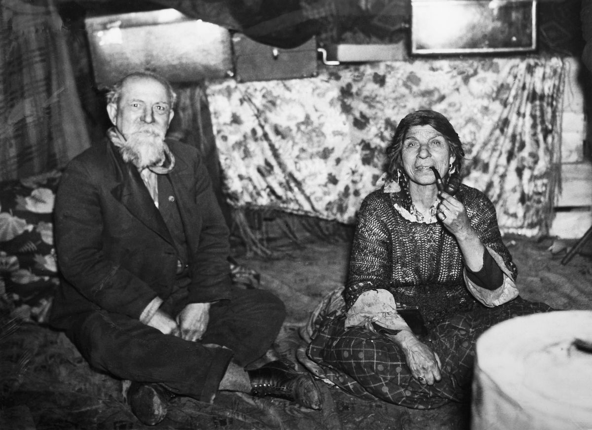 Ett romskt par sitter på golvet i sin bostad år 1963. Kvinnan röker pipa.