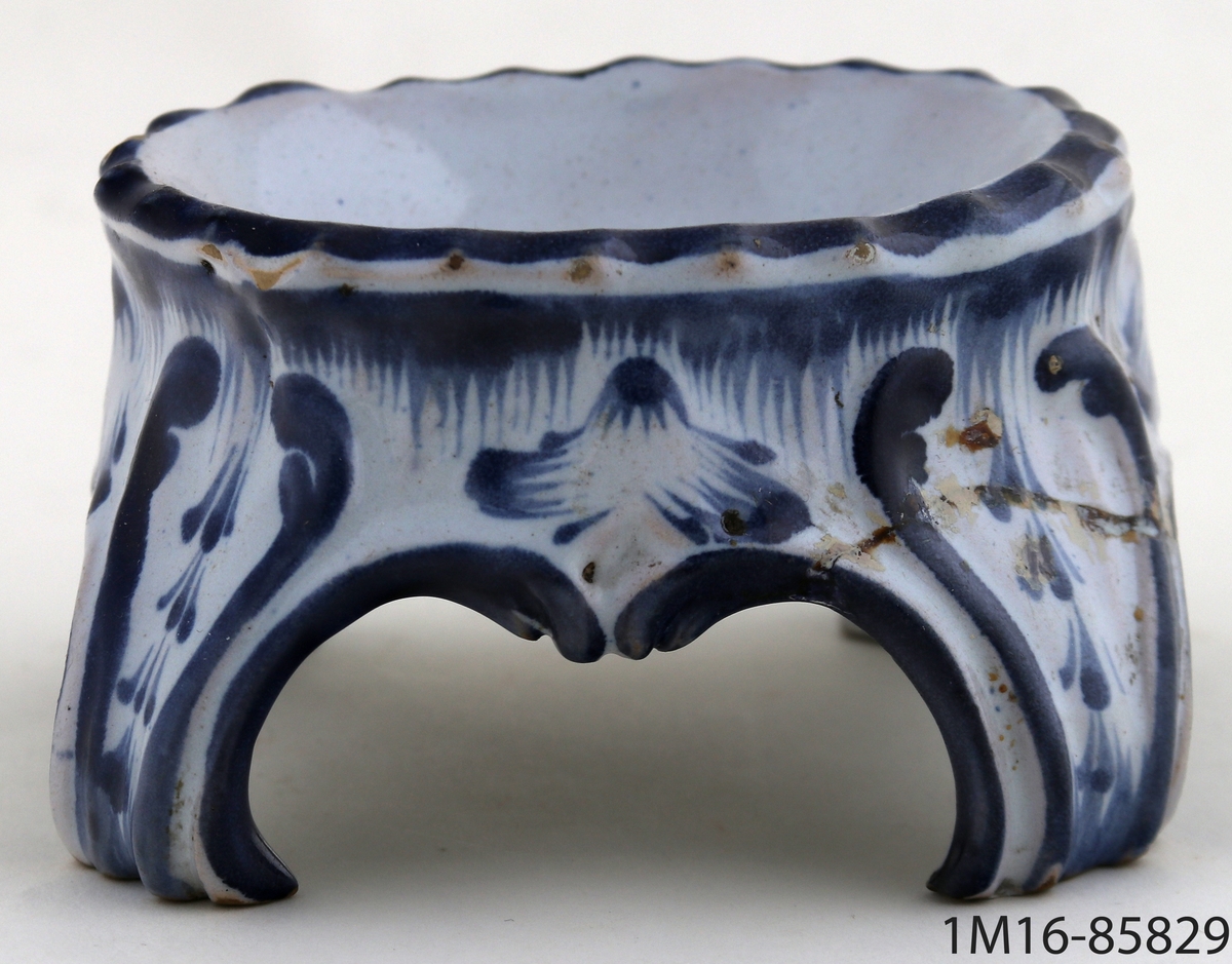 Saltkar, av vitt porslin med målad dekor i blått. Möjligen kinesiskt. Oval skålform med fyra svängda ben.