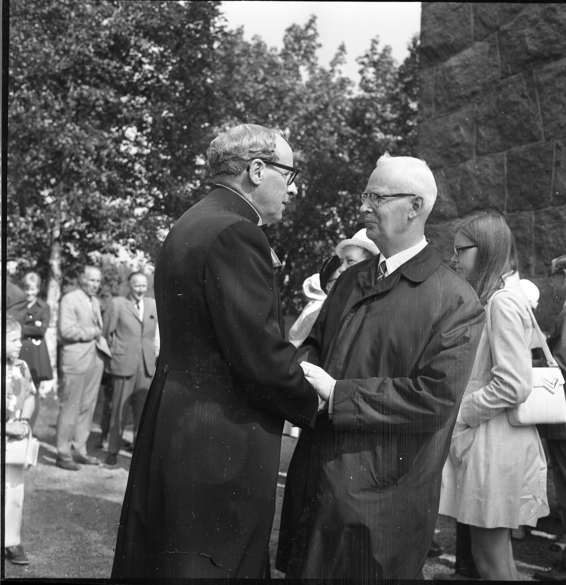 En prost utanför Lommaryds kyrka står och samtalar med en äldre man, de håller varandras händer.