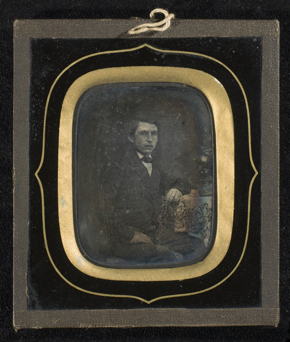 Daguerreotypi av mann som sitter ved et dukdekket bord.