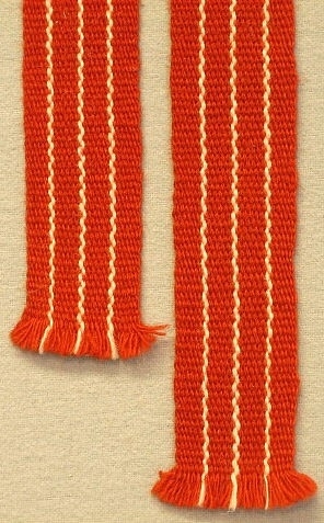 Uppvävd slips efter det lindade prov som A.Zorn gjort, Inv.nr 737:20.Brunröd botten med tunna vita längsgående ränder. Handvävda slipsar var en stor artikel på 1960- talet.