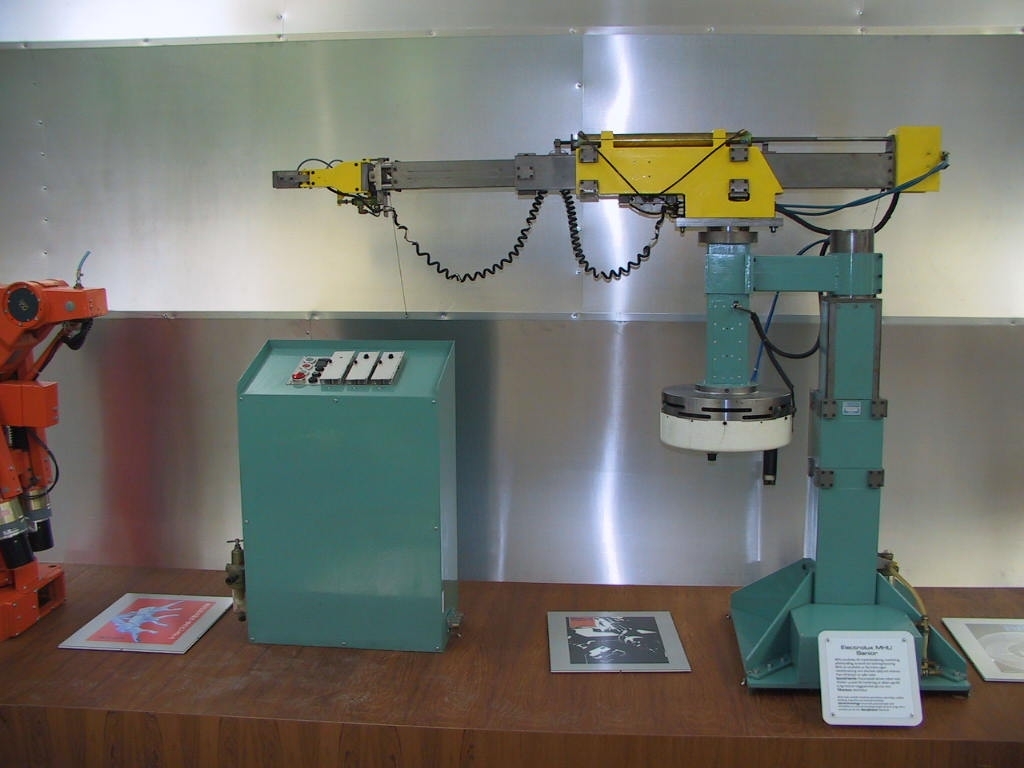 Industrirobot i stål och metall, som delvis är målad i gult och grönt. Till roboten finns också styr/programmerings-pulpet samt kopplingsdon. Roboten är uppbyggd av fyra funktionsmoduler: arm, tippenhet, rotationsenhet och pelare. Dessa är lätta att separera från varandra och kan användas var för sig eller i lämpliga kombinationer. Samtliga moduler är försedda med snabbkopplingar för el och tryckluft. Roboten är utrustad med ett elektro-pneumatiskt sekvensstyrt styrsystem. Roboten kan hantera laster upp till 10 kg.