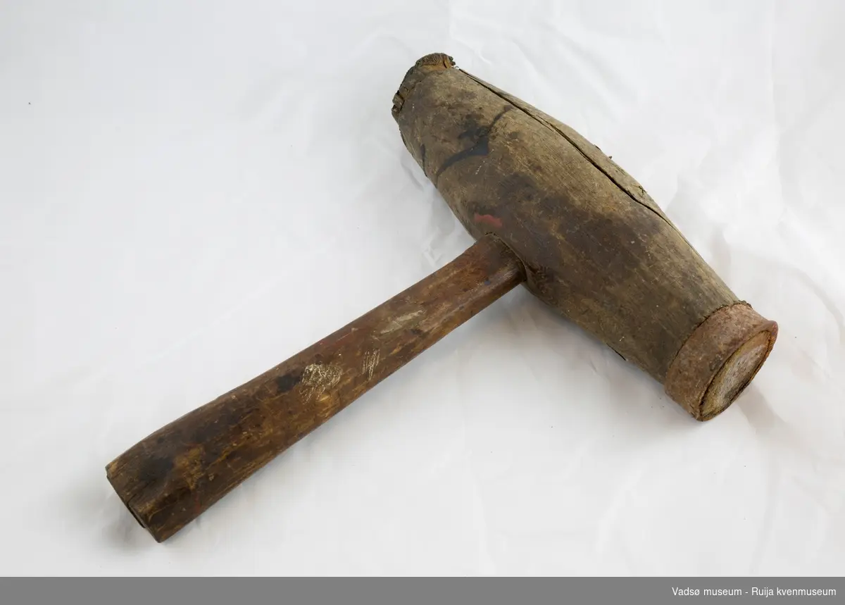 Sylinderformet hammer med skaft. Fortykket midtparti med ovalt skafthull. Hammeren smalner av mot endene. Det har opprinnelig sittet en jernring i hver ende, den ene mangler.