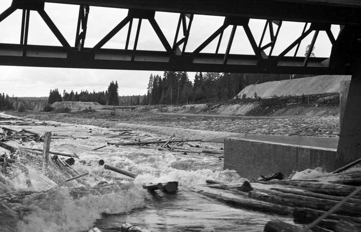 Tapping gjennom Osdammen i Valmen, der vannet fra Osensjøen renner over i elva Søndre Osa.  Bildet er tatt i 1941.  Det viser løpet i en betongdam, der det er et fall på cirka halvannen meter med et visst strømkav som får enkelte tømmerstokker til å reise seg.  Nedenfor aner en hvordan virket ble liggende, dels langsmed elvebreddene, dels på steinører ute i sjølve elveløpet. 

Den avbildete Osdammen - som i hovedsak er en betongkonstruksjon - ble bygd i 1938 som erstatning for en eldre dam der steinfylte tømmerkister hadde vært hovedelementer. 