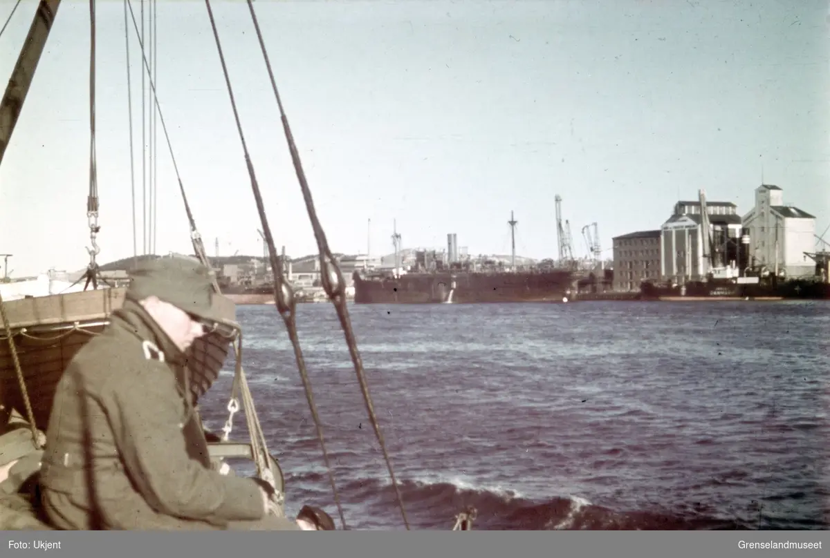 Havneområde med flere skip, kraner og bygninger. Skipet helt til høyre ser ut til å ha påskriften "Danmark".