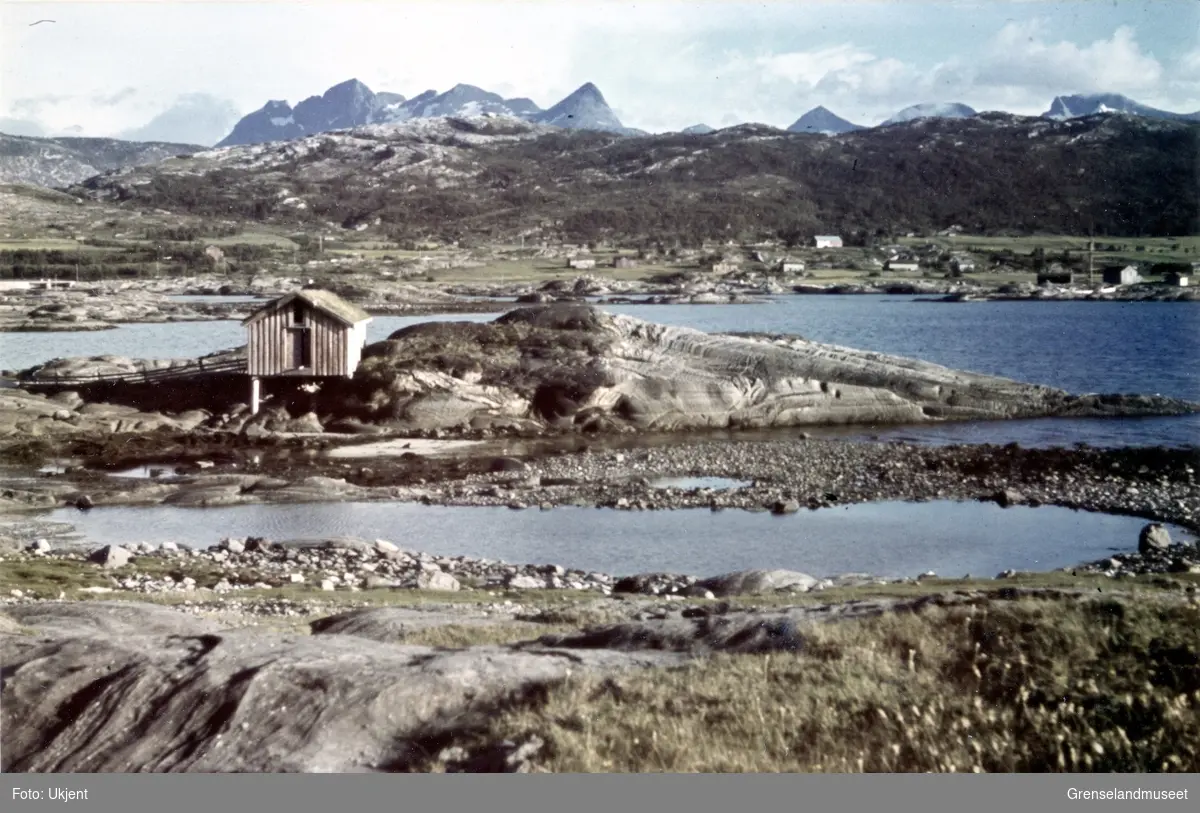 Motiv fra Saltenfjorden i Nordland. Bøvasstindan i bakgrunnen. Spredt bebyggelse midt i bildet.