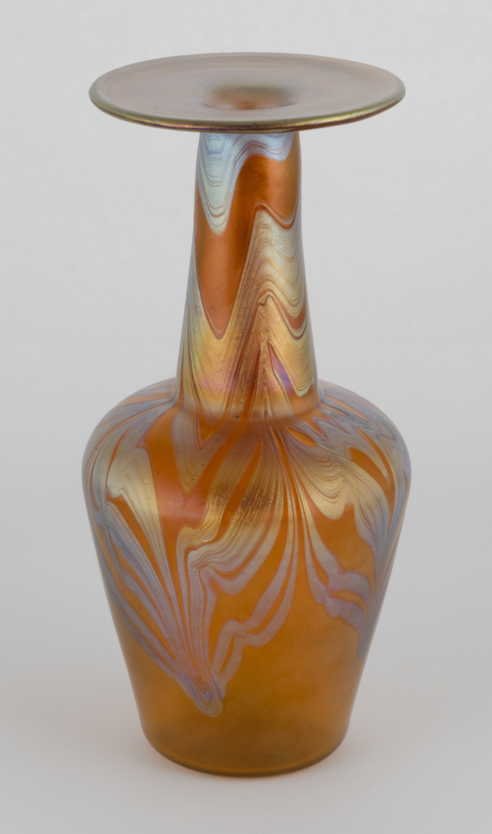 Balusterformet vase med høy hals. Gjennomskinnelig oransjefarget glass, dekorert med irisert organisk dekor på øvre del av korpus og den lange halsen. Overflaten til den brede, svakt trumpetformede munningsranden er helt irisert.