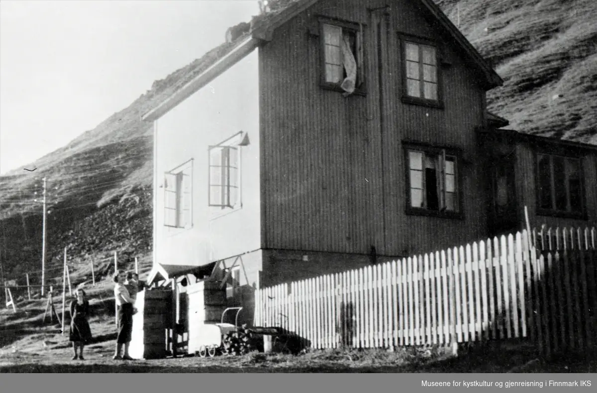 Honningsvåg. Harald Levangs hus på Bakken, sett mot Storfjellet. Stakittgjerde. Flere personer utenfor huset og et barnevogn.