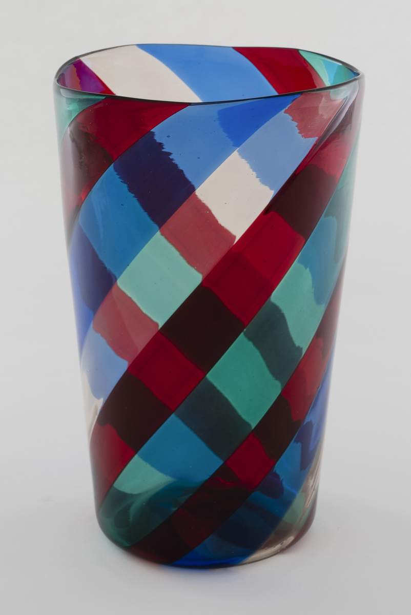 Tilnærmet sylinderformet vase i gjennomskinnelig polykromt glass. Vasen består av 2 cm brede bånd i rødt, grønt, blått og klart glass. Disse snor seg i en spiralbevegelse oppover korpus, og skaper optiske fargevirkninger i glasset. Ujevn sirkulær munningskant.