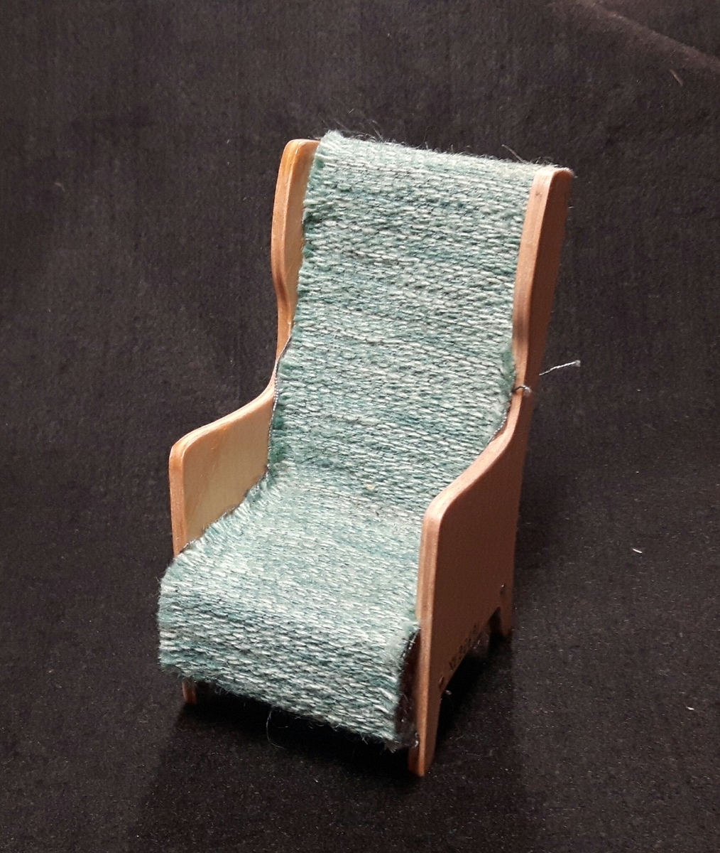 Karmstol med blågrå klädsel.

Ingår i en samling möbelmodeller använd vid kurser i heminredning anordnade av Älvsborgs läns norra slöjdförening.