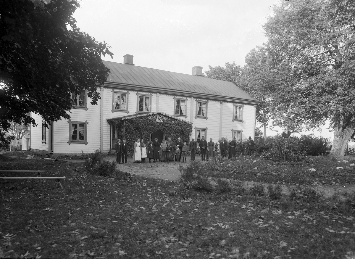 Familj ståendes framför okänt bostadshus, tidigt 1900-tal.