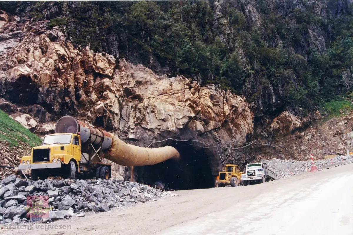 Ved bygging av Frafjordtunnelen 1995. Ventilasjonsvifte for tunnelarbeid er plassert på en Volvo N lastebil. I bakgrunnen står Caterpillar hjullaster og en Volvo N tippbil. Sprengt stein.