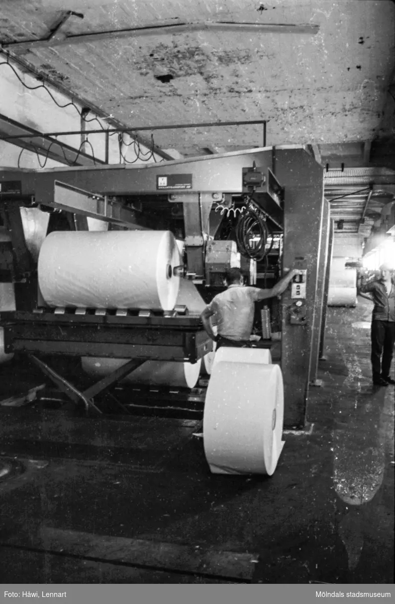 Män i arbete vid maskin på pappersbruket Papyrus i Mölndal, hösten 1970. Klipp 5 (arkmaskin), från baksidan, där man lade rullarna. byggnad 10.