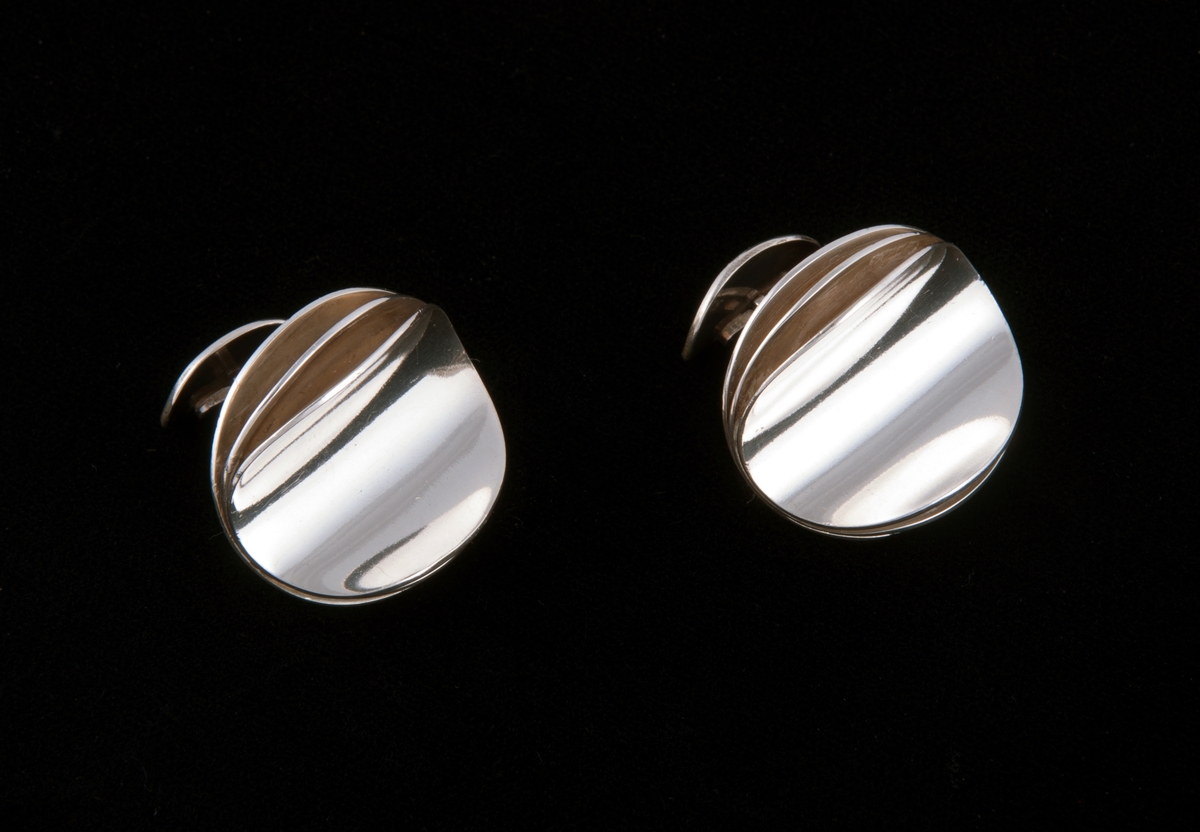 Består av tre like store sirkulære sølvringer som er satt sammen langs en midtakse. På hver siden av aksen er ringene bøyd oppover i ulik grad, symmetrisk på hver side.