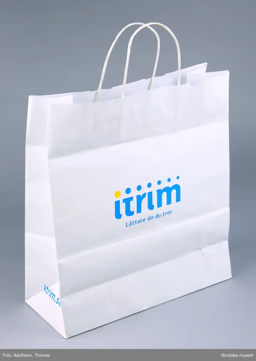 Inköpskasse, av vitt papper med å ena sidan Itrims logotyp, å andra sidan prickig dekor i gult och blått.