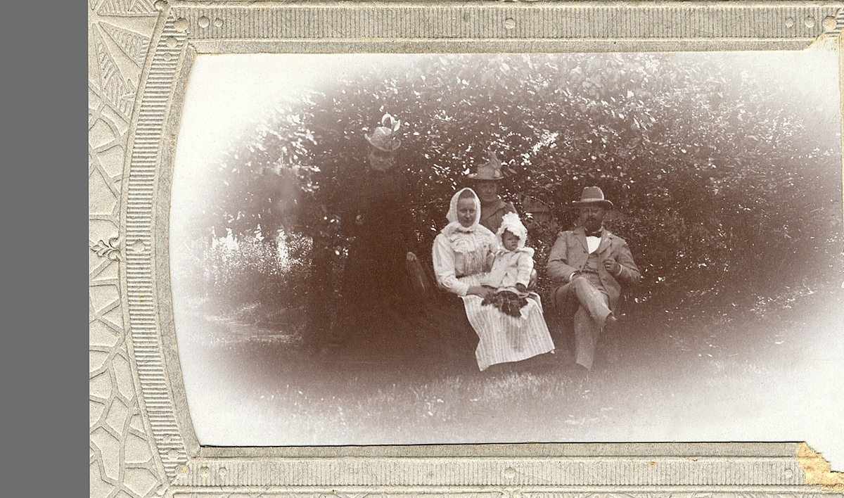 En man med tre kvinnor och en baby i en trädgård. 

Troligen Edvard Andersson (1875-1934) med sina systrar, en barnpiga och Edvards dotter Kristina (Stina), i trädgården till Edvards barndomshem, Kårestad Hansegård, Furuby.