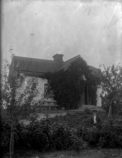 Bostadshus i trädgård samt kvinna, ca 1910.