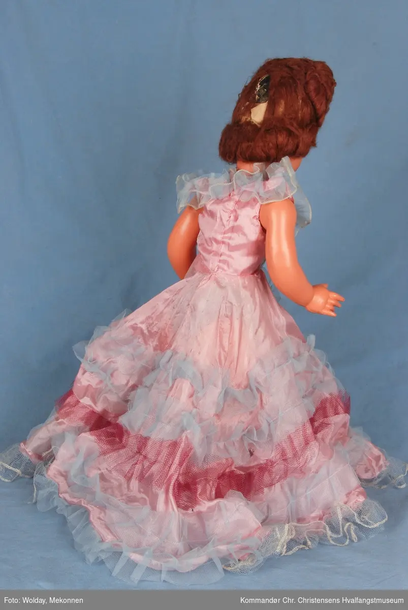 Rosa kjole med lyseblå og mørkrosa tyll. 
Brunt oppsatt hår. Mørk rundt øynene.
Dukken mangler sko. 
Arm, ben og hode er bevegelig. Dukken har hull i magen for en lydboks, selve boksen mangler. 

