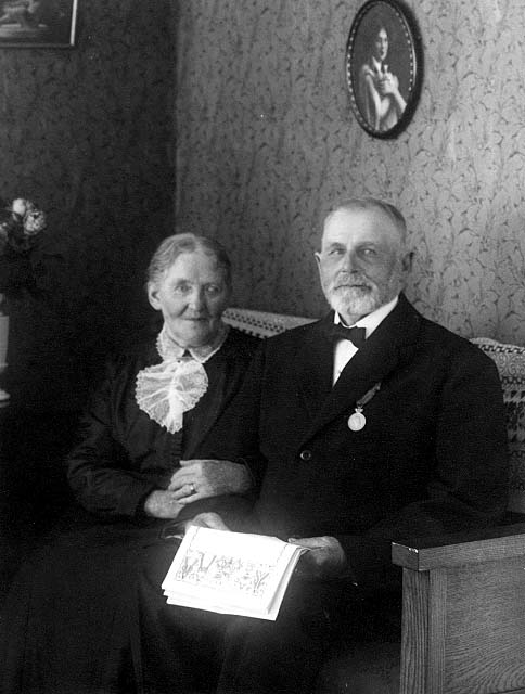 Äkta paret Emma och Karl "Hamnjohan" Johansson sitter i en soffa, sannolikt i sitt hem. Hon håller sin arm om hans. Han har en medalj på kavaj och håller telegram i handen. De firar guldbröllop.