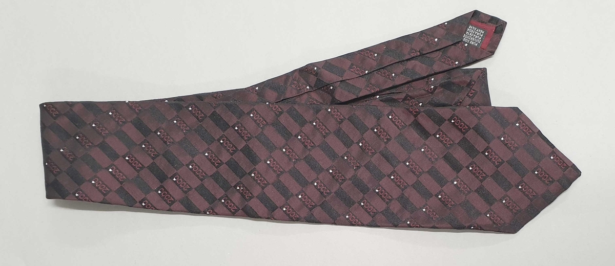 Fiolett slips i silke dekorert med tallet 2000 og små glassperler. Prislappen er festet til slipset.