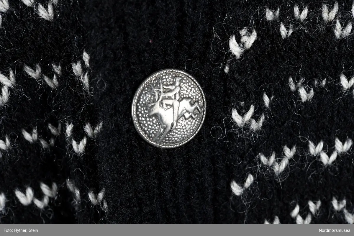 Strikkejakke / kofte i svart og hvitt mønster. 8 sølvknapper med figur av en person som rir på et reinsdyr.