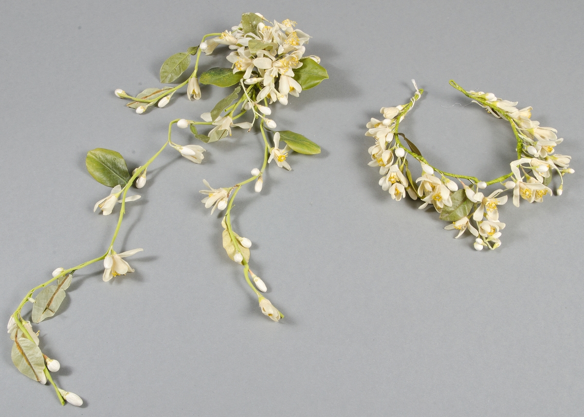 Girland längd ca 50 cm. Krans diameter ca 16 cm. Vita och orange blommor och gröna blad av vitt skinn och vaxat tyg.


