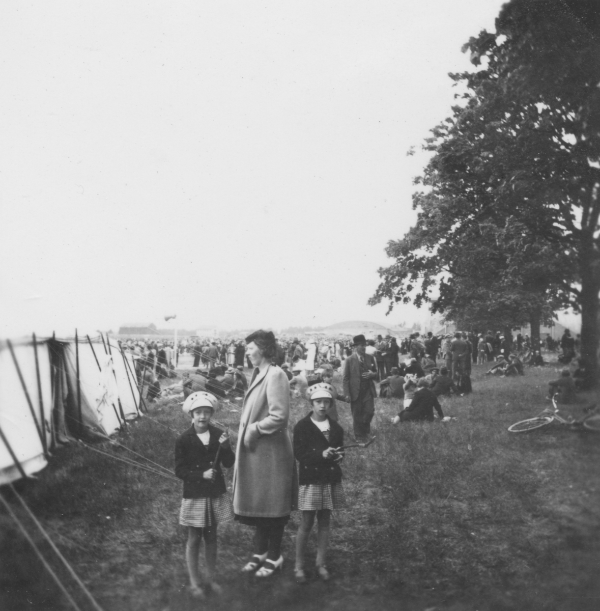 Publik vid flygdagen Flygets dag på Malmen, 1938. I förgrunden står en kvinna och två flickor bredvid ett tält.