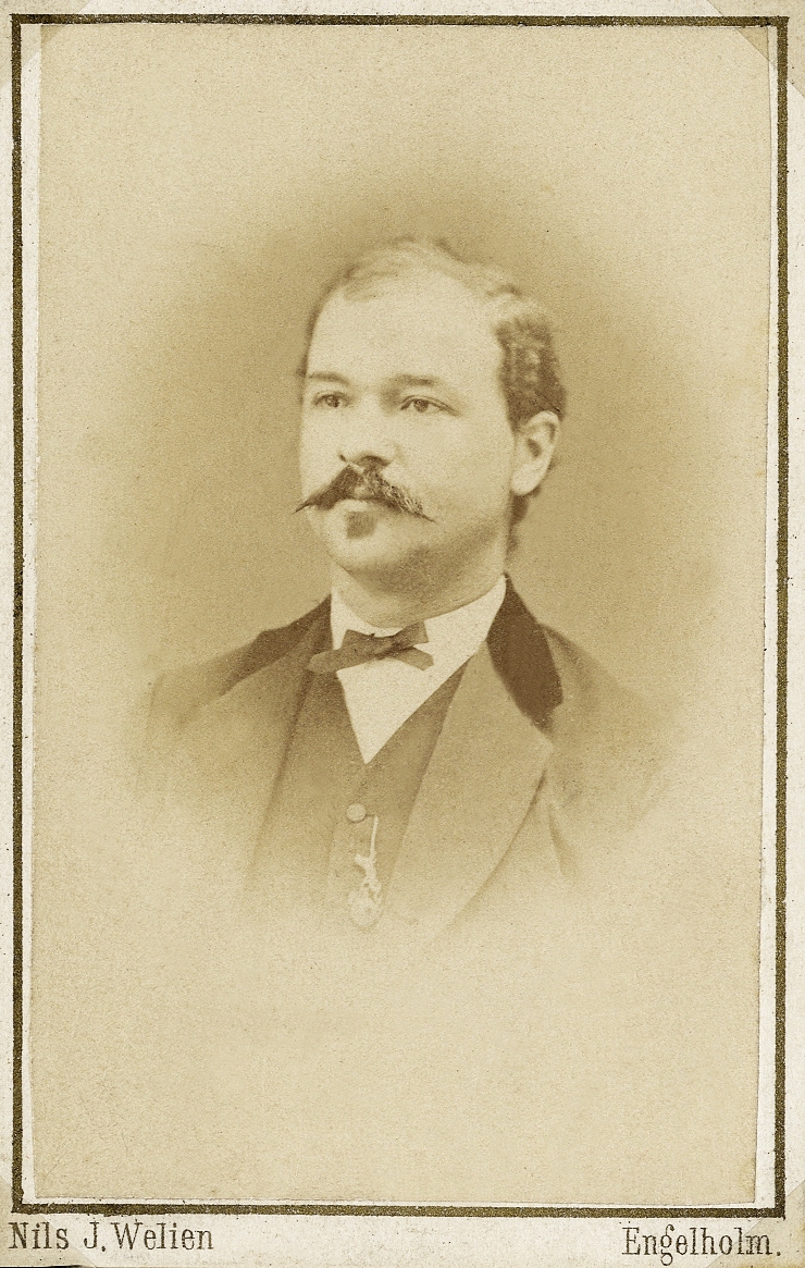Porträttfoto av en man i kavajkostym med sammetskrage, väst, stärkkrage och fluga. 
Bröstbild, halvprofil. Ateljéfoto.