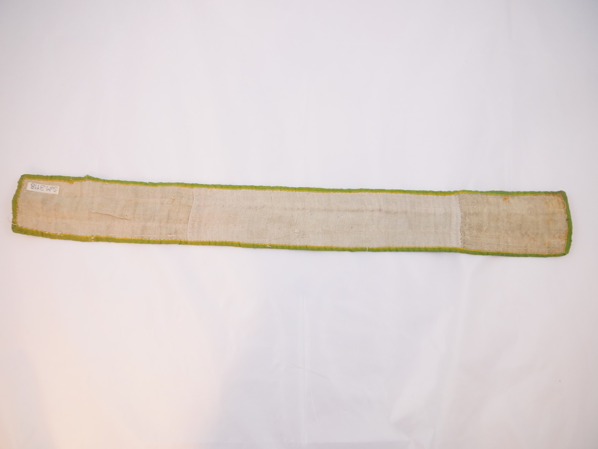 Breitt belte med brei forgyllt metallbord i midten. Heile beltet kvarda med grøn silke. Bakside av grov lin. Beltet er skøytt med ein ca 11 cm. lang del