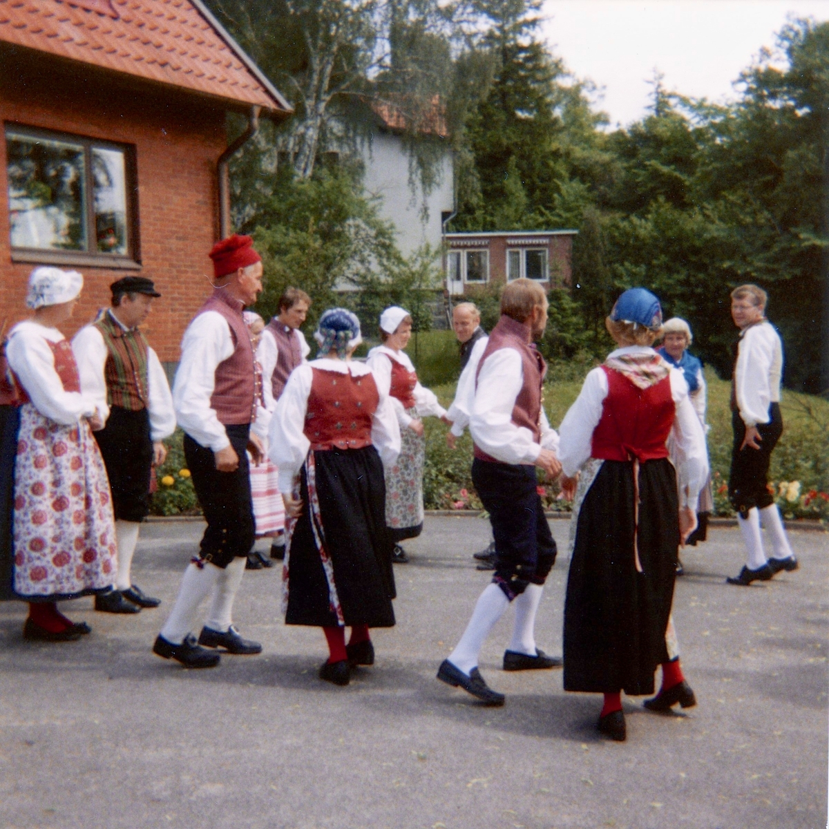 Midsommar och underhållning av Hällesåkers Folkdanslag utanför ålderdomshemmet Brattåshemmet 1980. Dansparen är folkdräktsklädda. Relaterat motiv: A1878.