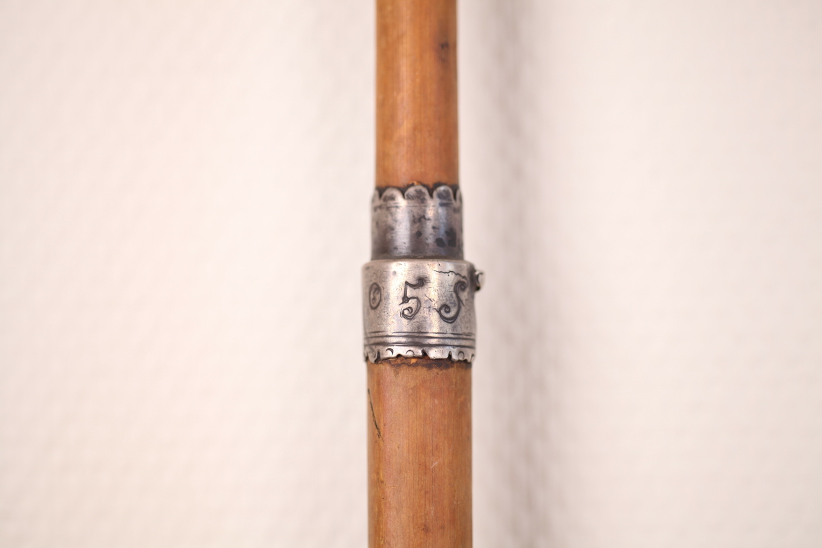 Dreid håndtak, to ringer av metall, den ene ringen er rett under håndtaket, den andre ringen er litt over midten av stokken. Den andre av ringene har følgende inskripsjon I L 80105 S. Muligens er stokken del av en ødelagt paraply.