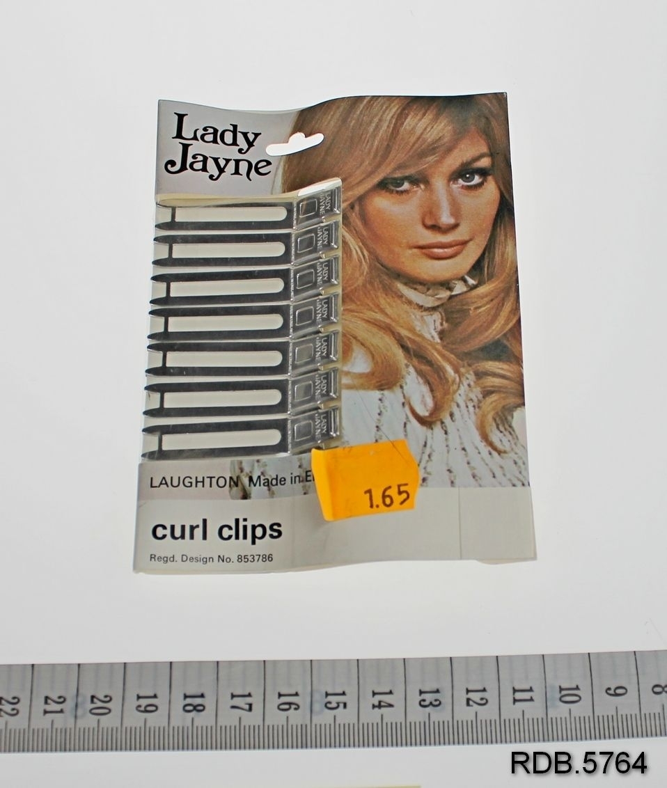 Et brett med 8 hårspenner (clips) merke Lady Jane. Clipsene er festet til en papplate, brettet som en konvolutt med plastvindu og bilde av en ung dame.