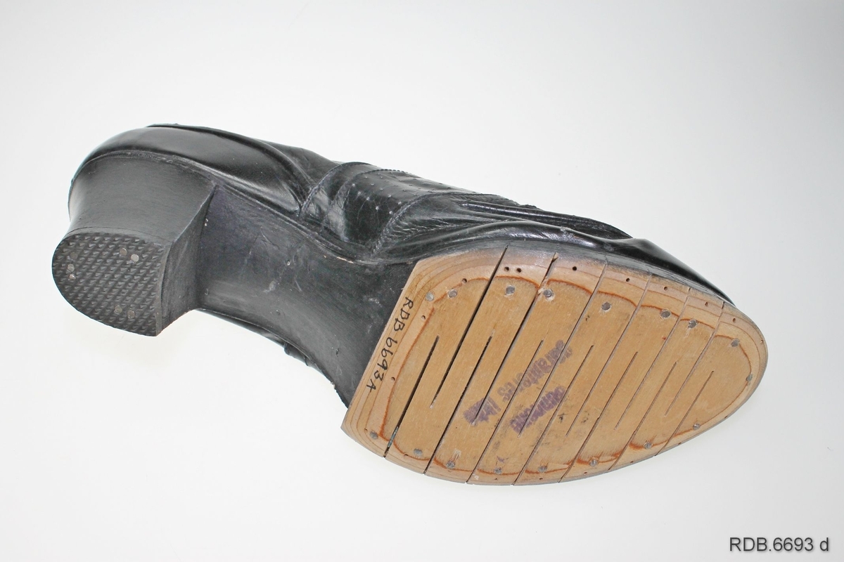 Et par svarte damesko med høge, kraftige hæler. Skoene er "krigsvare", fra 2. verdenskrig, med overlær av tynt stoff og plast og tresåler (trebunner) som er spikret på. Skoene har åpning foran med tunge og tre par hull med itredde svarte lisser. Under hælen er påspikret en gummisåle.