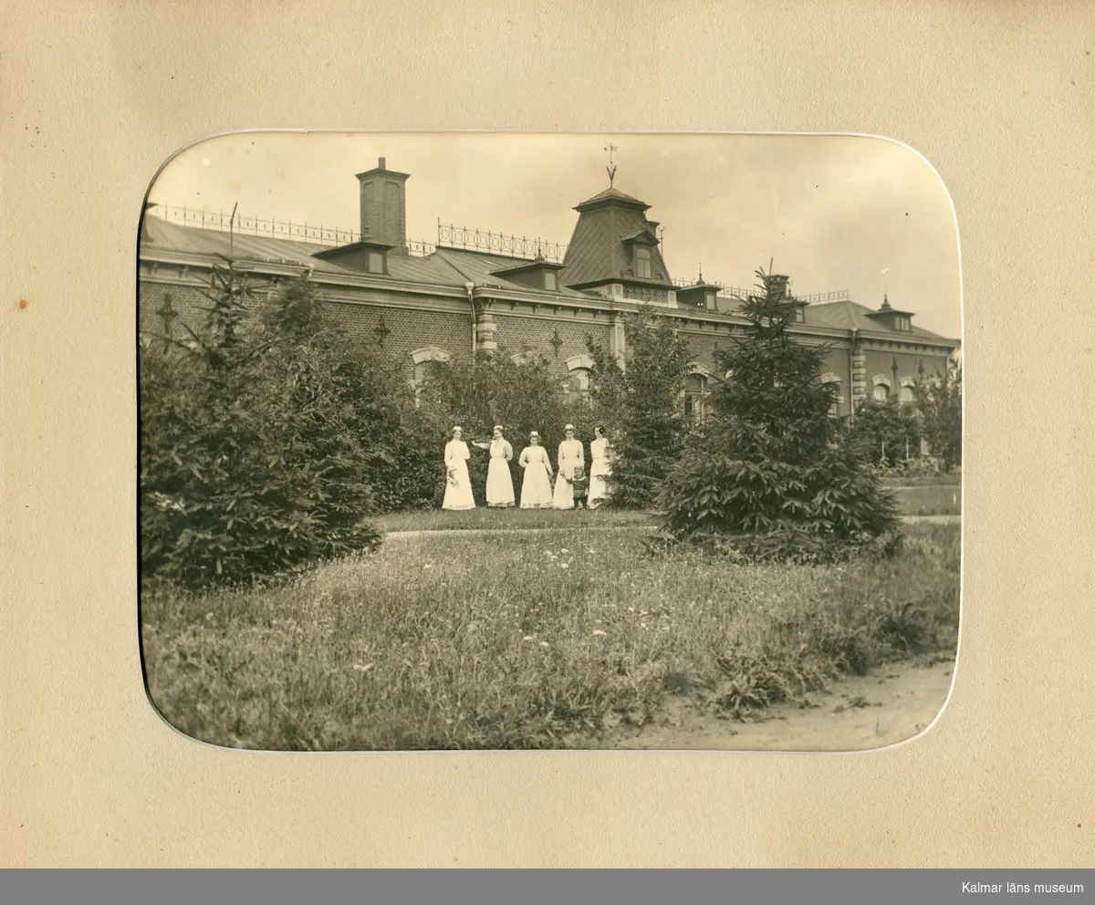 Motivet föreställer Epidemisjukhuset på Lindö i Kalmar. Framför byggnanden står fem kvinnor ur personalen samt ett barn. Kvinnan i mitten är givarens mormors syster Emmy Gustafsson, hon var föreståndare vid sjukhuset.