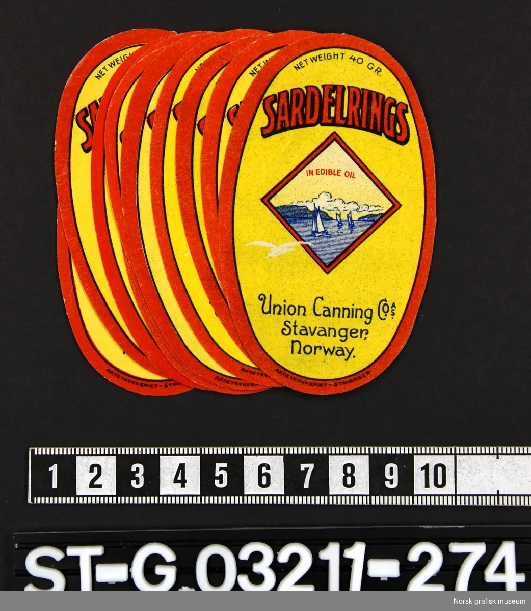 Mindre ovale etiketter i rødt og gult. Et motiv med seilbåter er midt på etiketten i en firkantet ramme. 

"Sardelrings in edible oil"