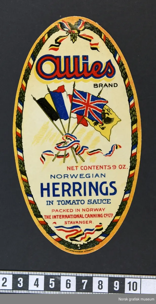 Oval etikett med fire vaiende flagg; belgisk, fransk, britisk og et gult med en tohodet ørn. 

"Norwegian herrings in tomato sauce"