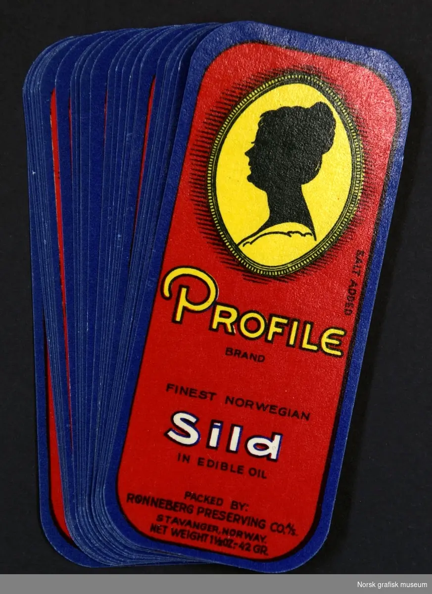 Små etiketter med rød bakgrunn og ramme i mørk blå. Over varemerket vises en sort kvinnesiluett i en gul ramme. 

"Finest Norwegian sild in edible oil"