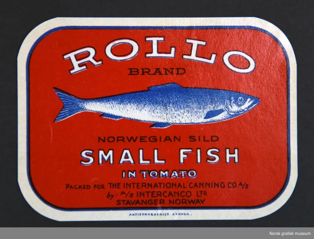 Rød etikett med en illustrasjon av en fisk midt på. 

"Norwegian sild small fish in tomato"