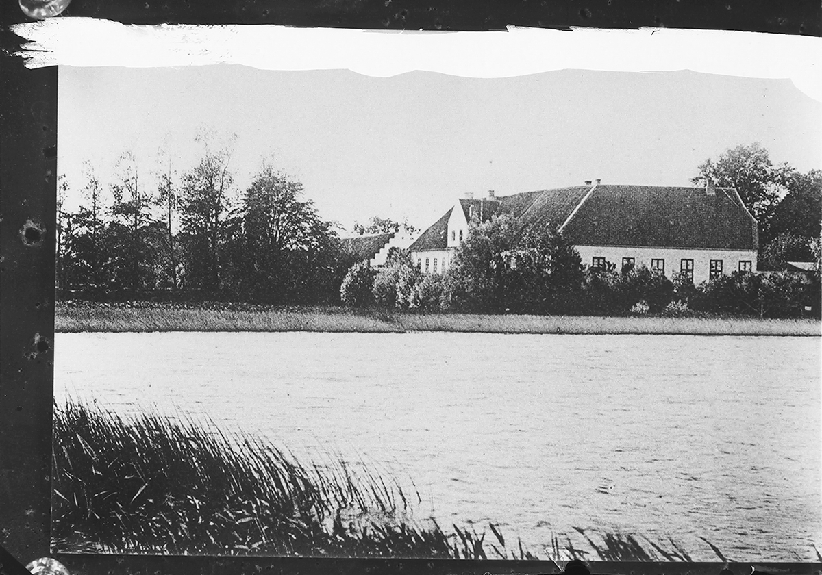 Byging ligger ved et lite vann. Fotografert 1925.
