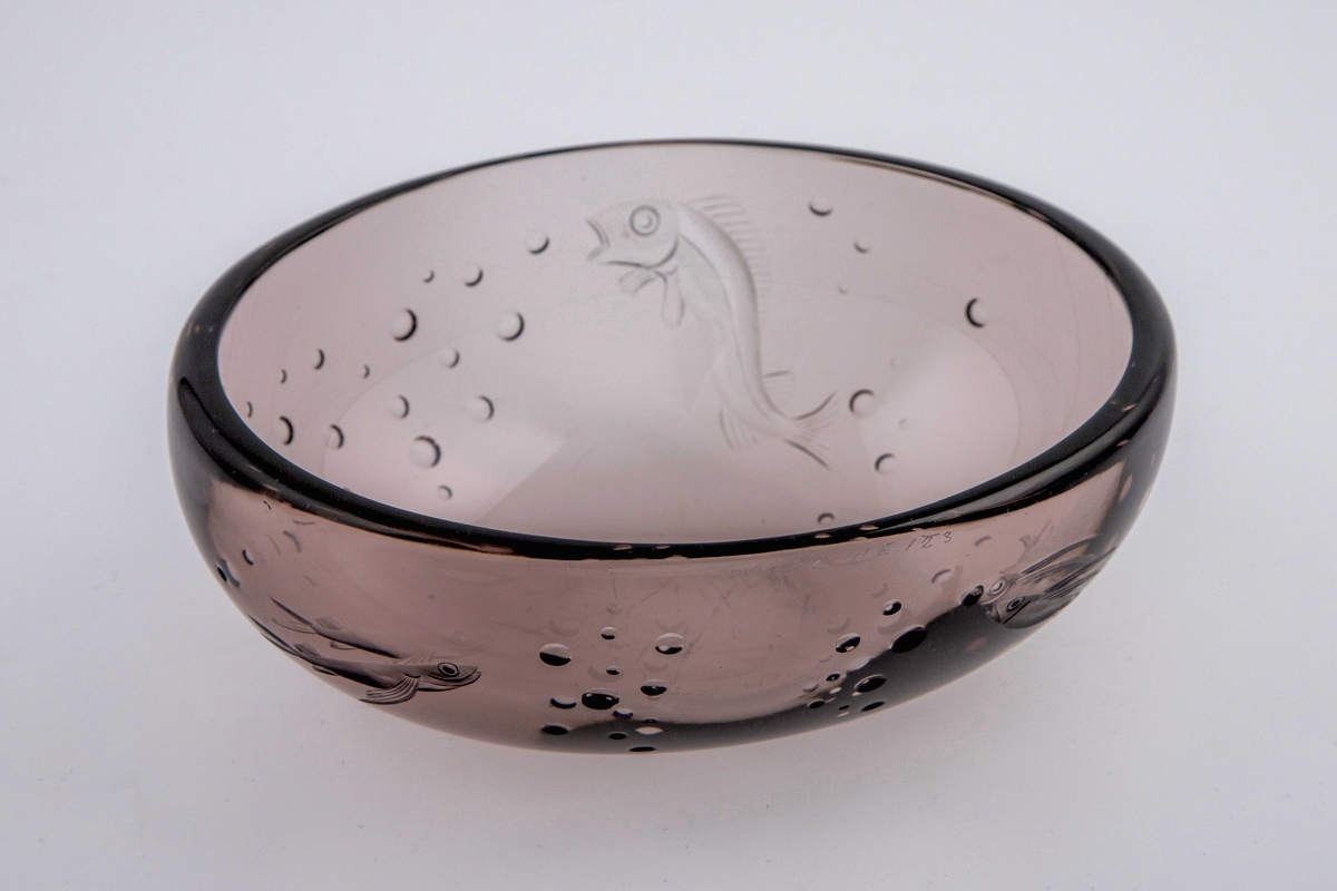 Ovalformet skål i røkfarget gjennomskinnelig glass. Korpus er dekorert med sliping, i form av fisker samt luftbobler.